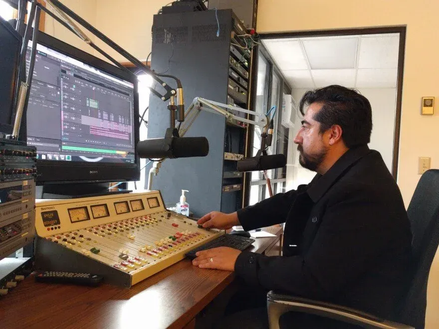 A man sits in front of a sound board and microphone while measuring levels on his computer