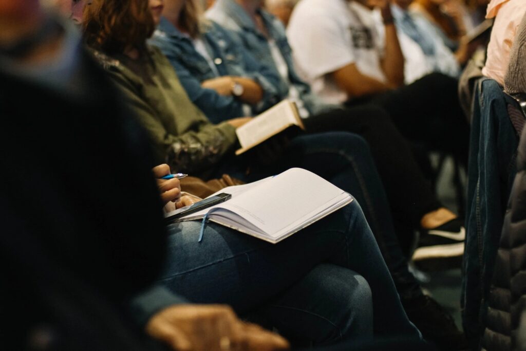 A group of people sitting side by side taking notes on notebooks in their laps