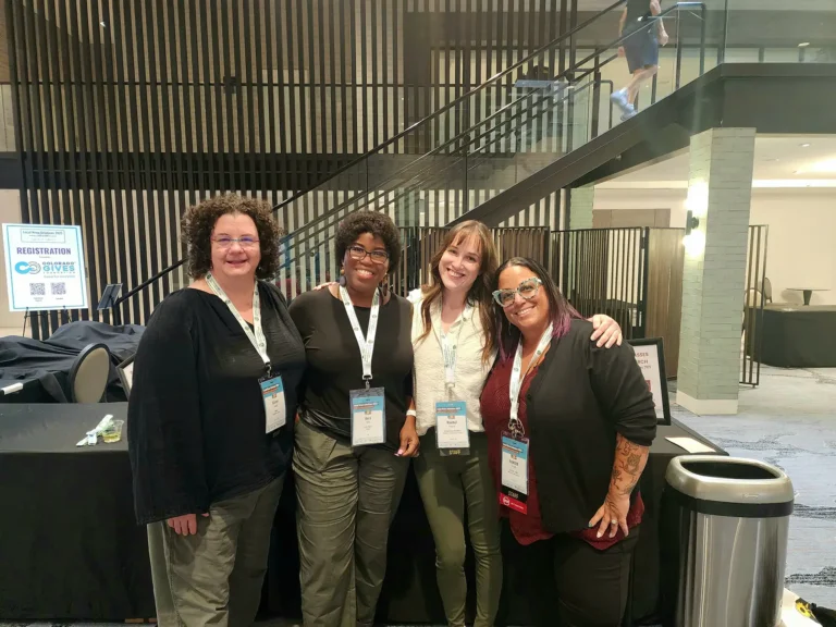 A group of women wearing lanyards gathered in front of a registration table