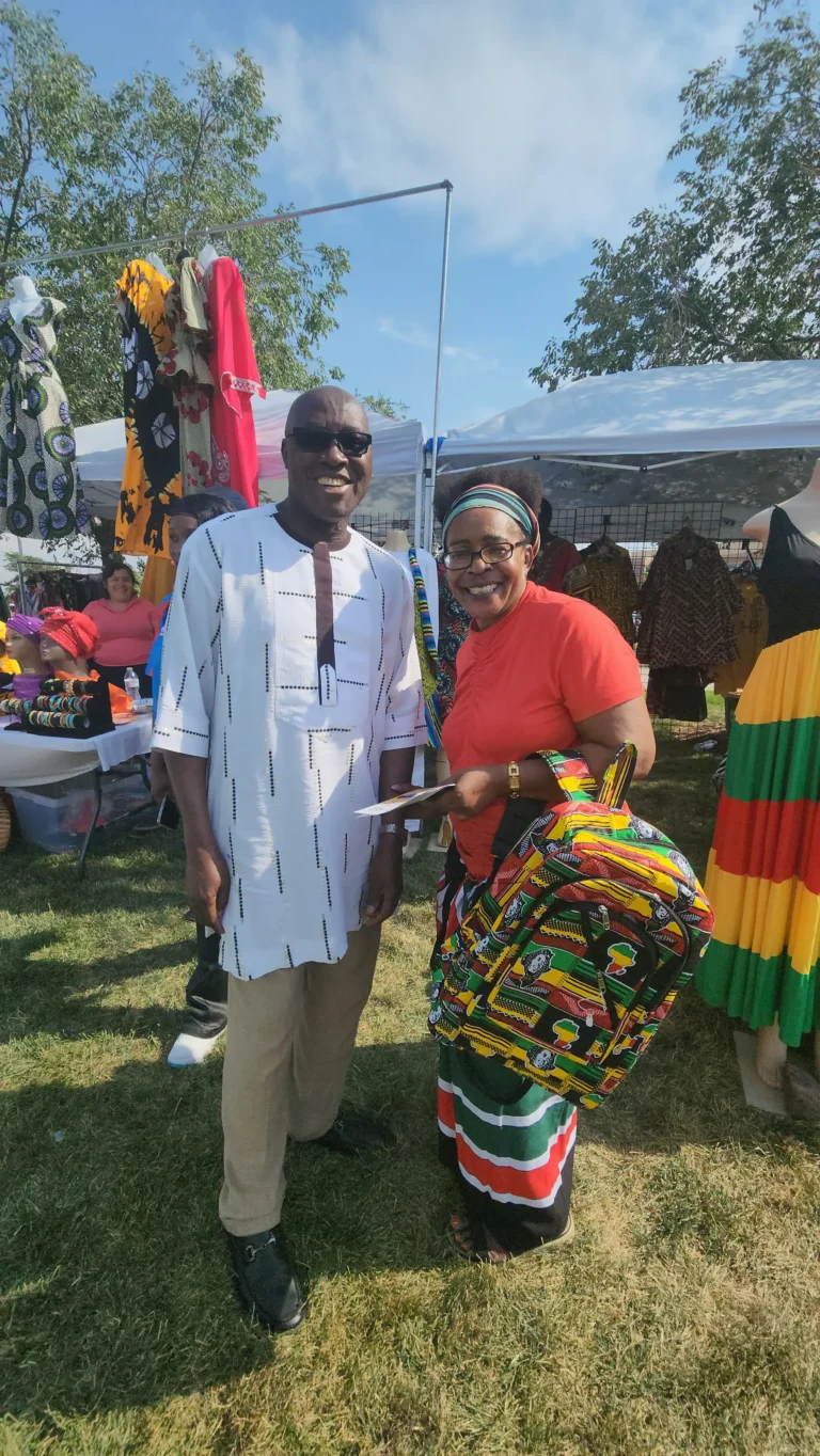 A black man and woman wearing African inspired clothes and accessories at an African market