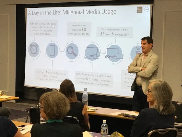 A man speaks in front of a classroom with a presentation being projected that reads "A day in the life: millennial media usage"