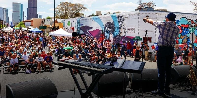 A man on a stage points out at a crowd on a street on a sunny day